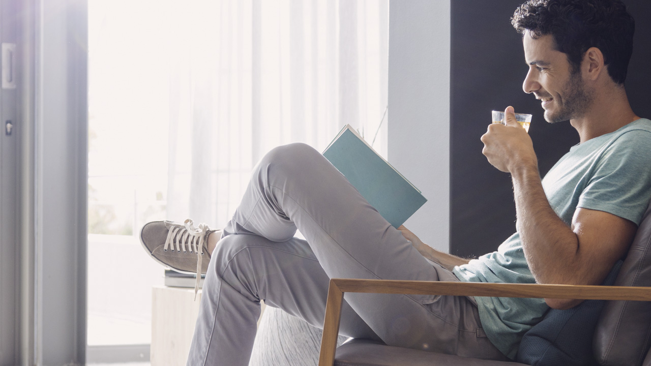 Man sitting in armchair drinking coffee reading