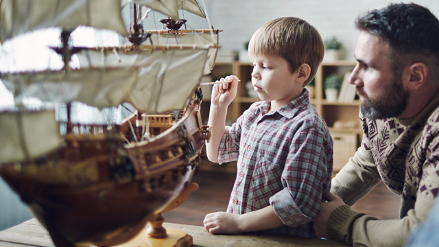 Far og sønn hjemme som ser på en gammel miniatyr båt. 