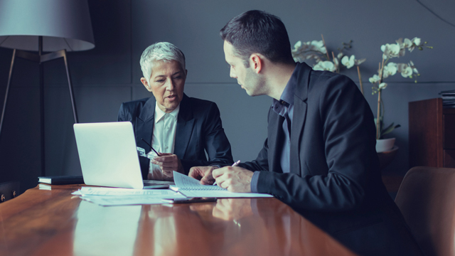 Two people in a meeting in front of a computer and a pile with paper