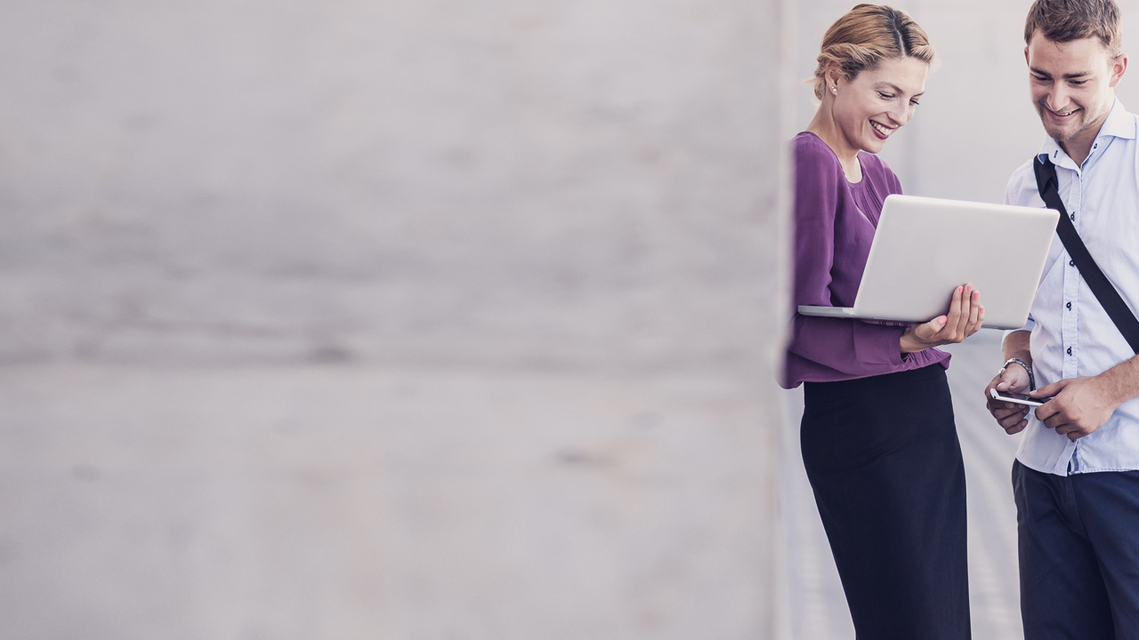 Two persons meeting outside an office are looking at a laptop 