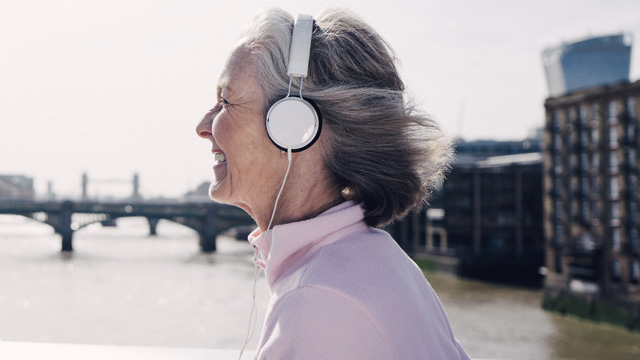 Smilende voksen dame med hodetelefoner smilende på tur utendørs i en storby. 